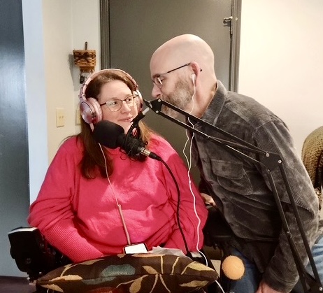 Jennifer and Dan Digmann sit close together sharing a microphone while recording their podcast about living with Multiple Sclerosis and faith.