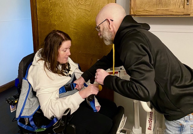 Dan assisting Jennifer with a transfer using a sit-to-stand harness at home, illustrating daily family caregiving