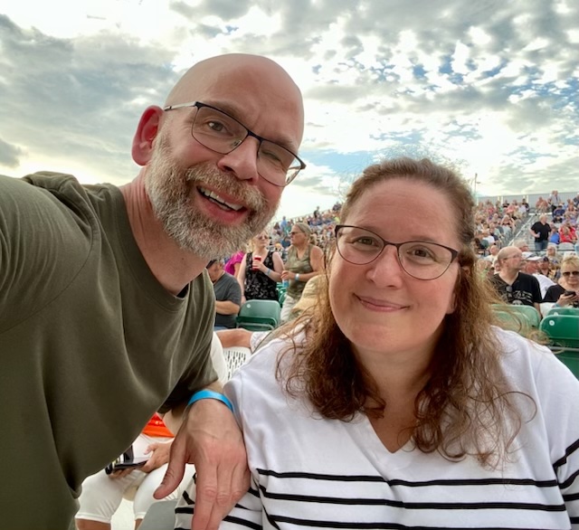 Dan and Jennifer Digmann smile together at an outdoor concert venue, reflecting their love of live music and the importance of accessible seating.