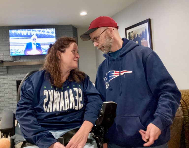 Jennifer and Dan Digmann watching football together while wearing Seattle Seahawks and New England Patriots gear.