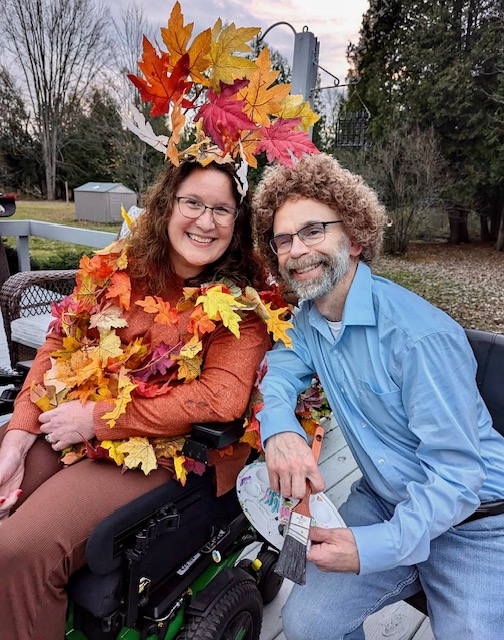 Dan dressed as Bob Ross beside Jennifer dressed as his colorful “happy little tree” for Halloween.